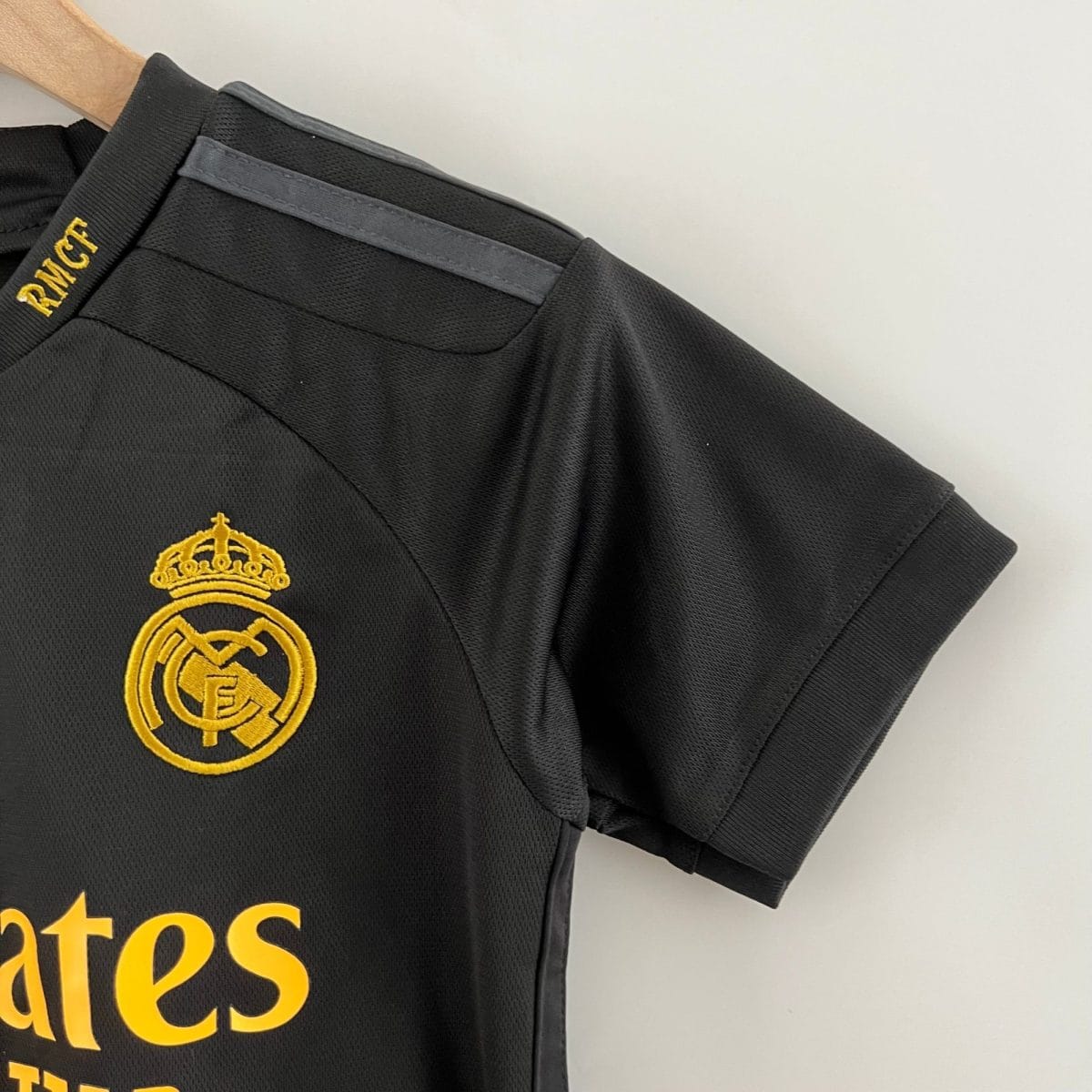 Close-up of a black polo with a gold Real Madrid crest embroidered on the chest.