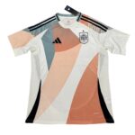 White soccer jersey with peach and teal geometric panels, Adidas logo, and national crest on the chest.