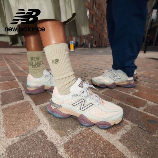Close-up of two people wearing pastel New Balance sneakers and beige crew socks on a brick sidewalk in an urban street setting, logo visible on shoes and socks.