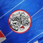 Round embroidered patch on blue fabric featuring a black-and-white abstract mountain design inside a white circle with a red border.