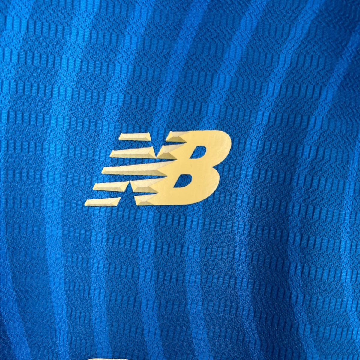 Close-up of blue knit fabric with a partial yellow letter visible at the bottom edge, textured pattern evident.