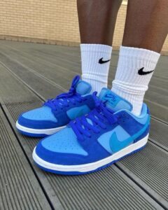 Blue Nike sneakers with matching laces and a white sole, worn with white Nike socks on a wooden deck
