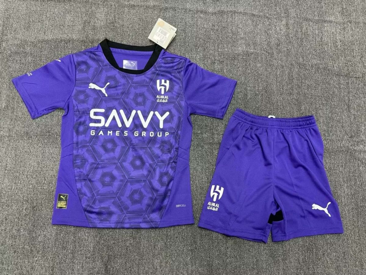 Purple soccer jersey with matching shorts on a gray carpet; hexagonal pattern, white Puma logo, Alhilal crest, and SAVVY GAMES GROUP sponsor text.