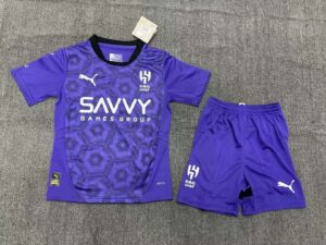 Purple soccer jersey with matching shorts on a gray carpet; hexagonal pattern, white Puma logo, Alhilal crest, and SAVVY GAMES GROUP sponsor text.