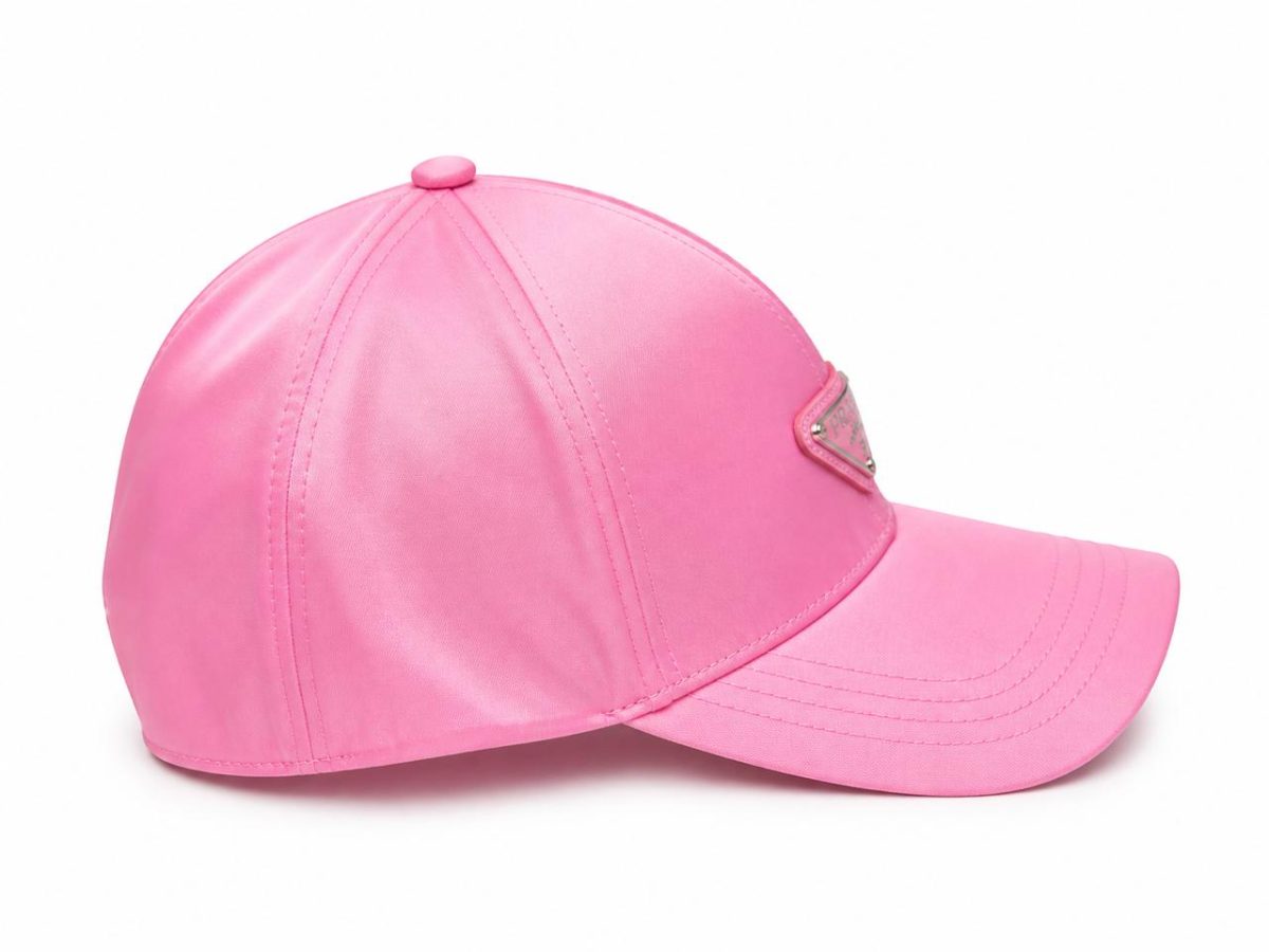 Pink baseball cap with a curved brim and a small metal emblem on the front, set against a white background.