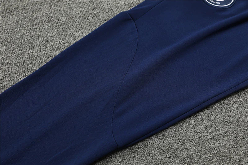 8780a83c_1024x1024_2x_e72f0912-d6d7-4cc8-8088-25f9f91d4b10 | UAE SPORT STORE Navy blue jacket sleeve laid flat on gray carpet, with a small circular logo patch at the upper edge.
