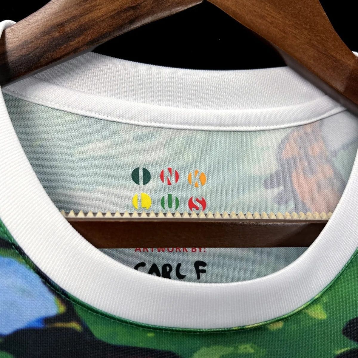 Close-up of a shirt collar on a wooden hanger, revealing a multicolor 'ONE OF A KIND' design printed on the inside neck label.