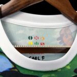 Close-up of a shirt collar on a wooden hanger, revealing a multicolor 'ONE OF A KIND' design printed on the inside neck label.