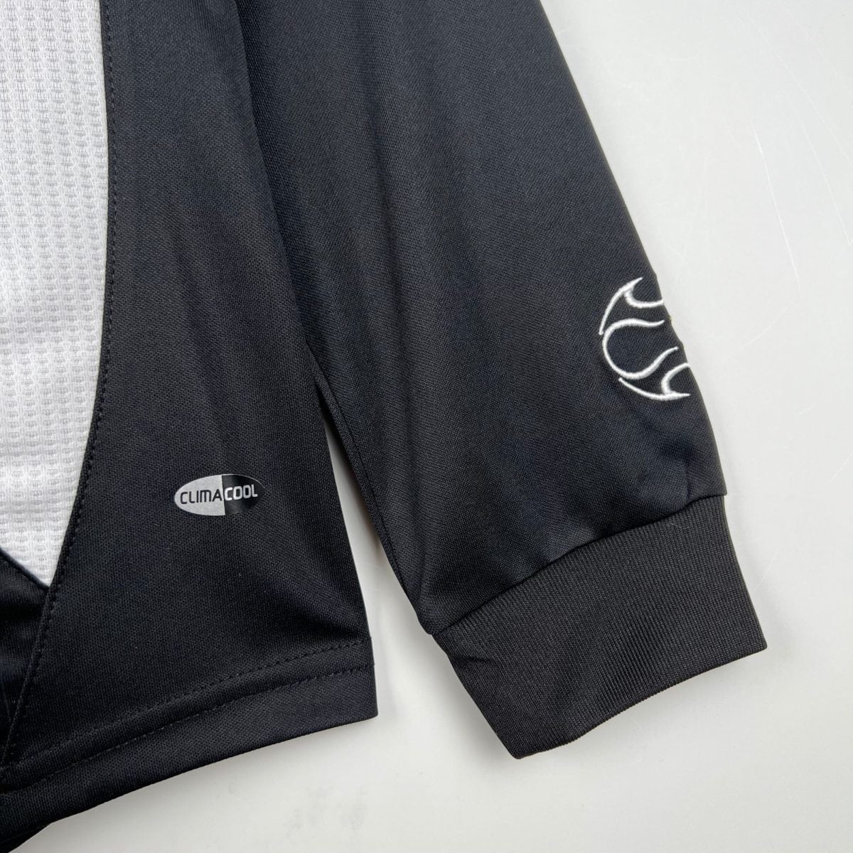 Close-up of black athletic fabric with a white embroidered design and a CLIMACOOL badge visible on the left.