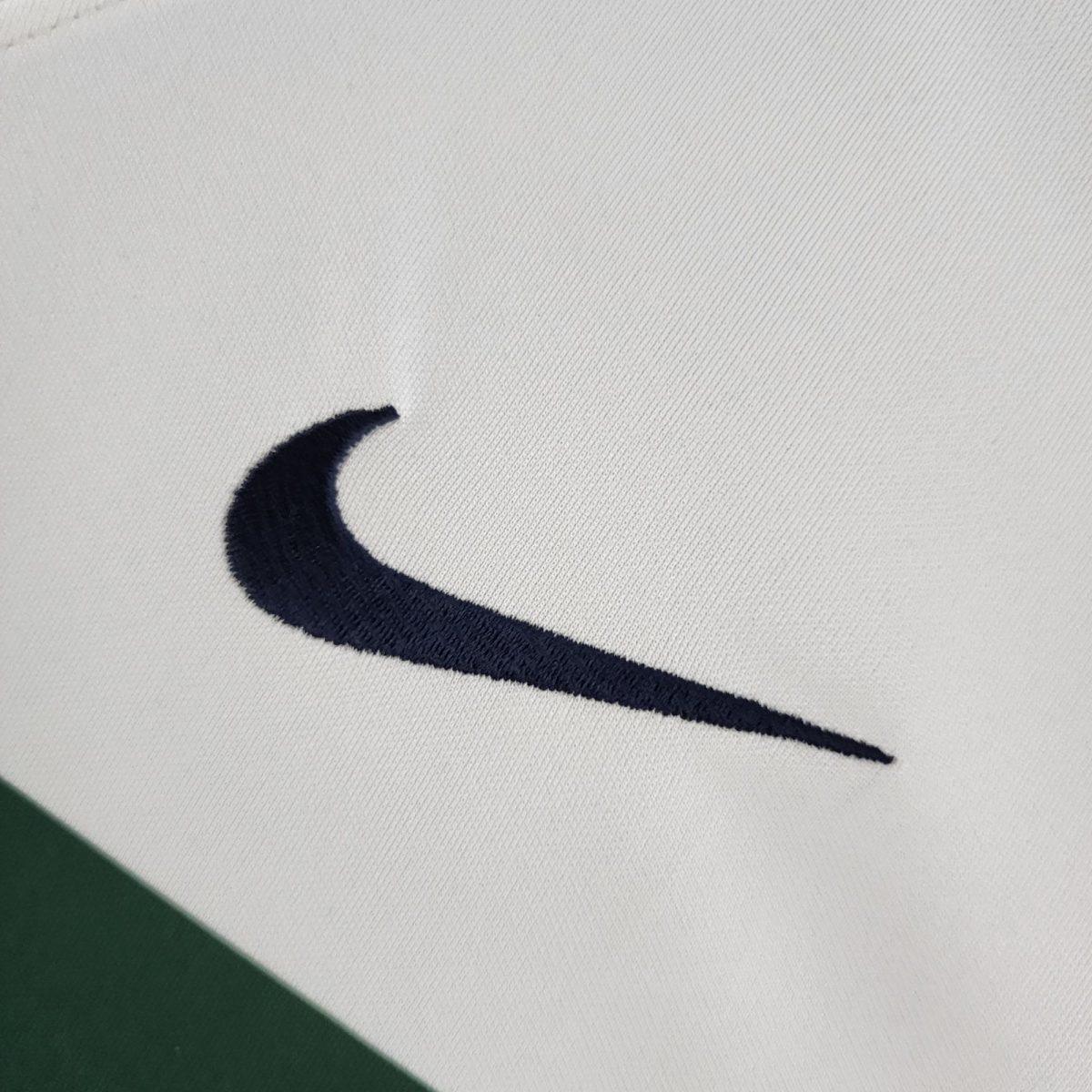 Close-up of white fabric with a dark navy curved stripe resembling part of a logo, and a green area at the bottom-left corner.