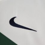 Close-up of white fabric with a dark navy curved stripe resembling part of a logo, and a green area at the bottom-left corner.
