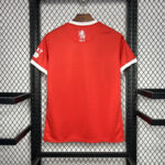 Back view of a red football jersey with white collar and sleeve cuffs hanging on a hanger, MFC crest near the neck.