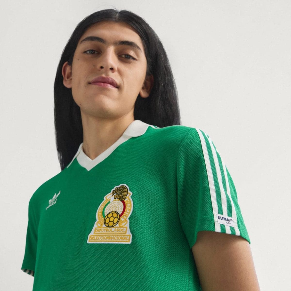 Portrait of a person wearing a green soccer jersey with the Mexican national team crest, looking slightly to the side and a neutral expression.