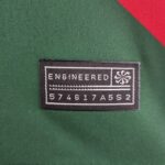 890e12ab_971adba7-d5a6-4c32-8b76-0256bf9f31af | UAE SPORT STORE Close-up of green fabric with a black rectangular label reading 'ENGINEERED' in white, bordered by white stitching and a red diagonal accent in the corner.