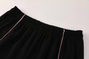 8940d585 | UAE SPORT STORE Black elastic-waist pants with pink piping along the side seams and pockets, close-up view.
