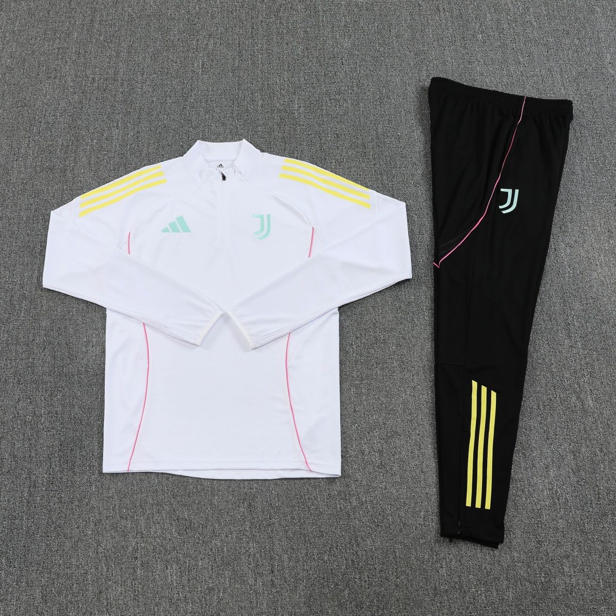 White Adidas athletic jacket with pale blue logo and yellow stripes on the shoulders laid beside black pants with neon yellow stripes, on gray carpeted floor.