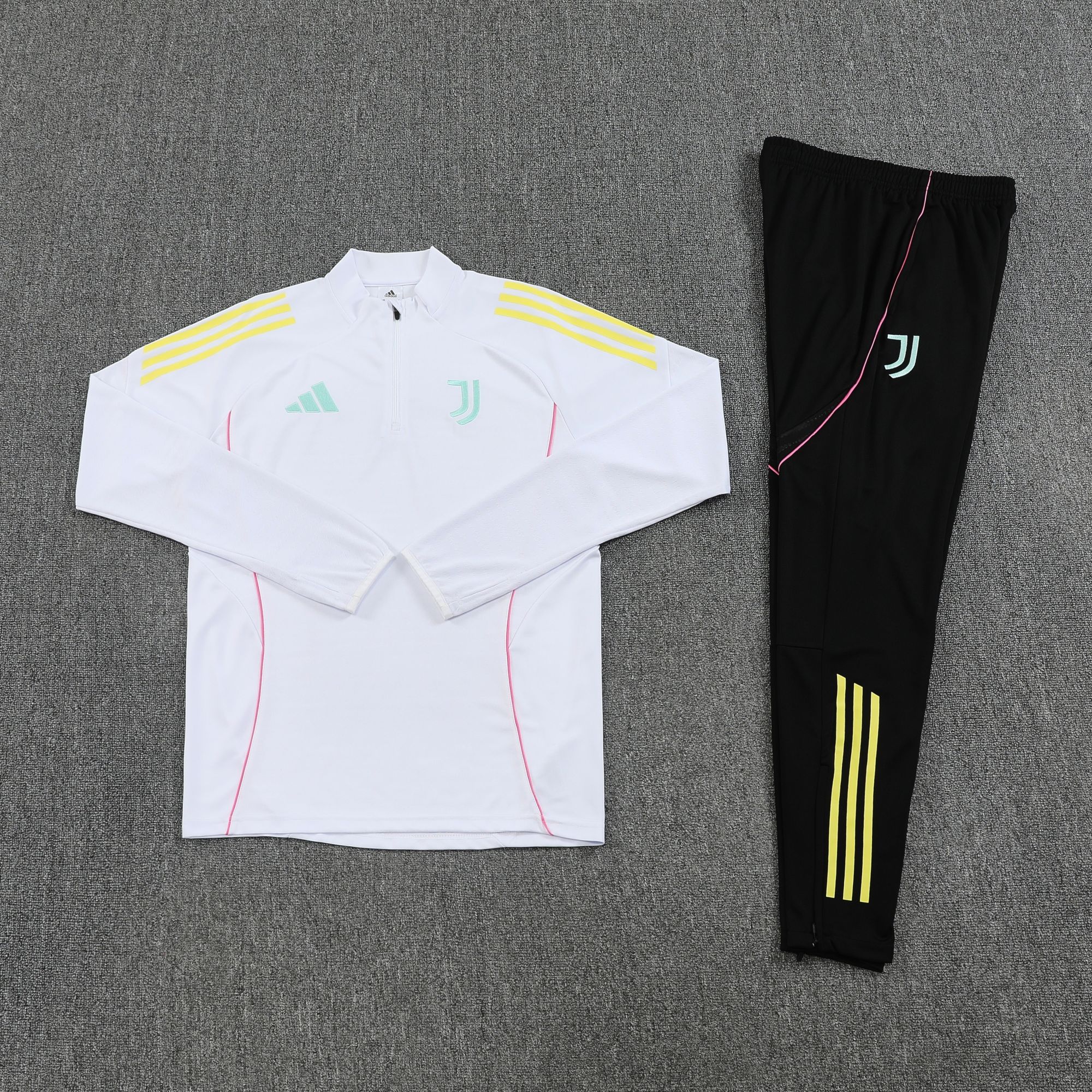 8942deeb | UAE SPORT STORE White Adidas athletic jacket with pale blue logo and yellow stripes on the shoulders laid beside black pants with neon yellow stripes, on gray carpeted floor.