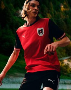 Soccer player in a red and black jersey running on a field, crest visible on chest.