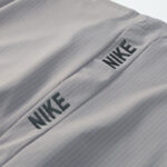 Light gray fabric with a stitched seam and two Nike logos along the seam, showing branded athletic material.