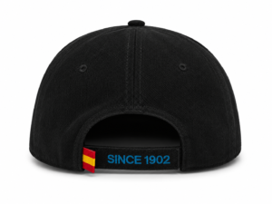 Back view of a black baseball cap with an adjustable strap, featuring blue 'SINCE 1902' embroidery and a small red-yellow flag tab