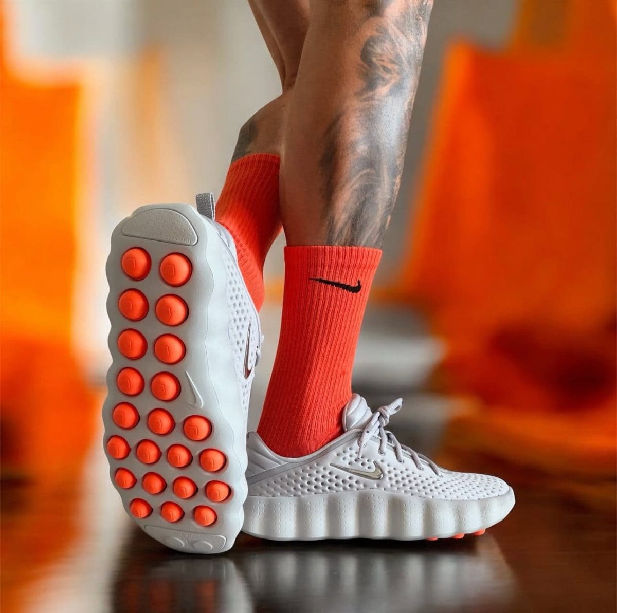 Close-up of a white athletic shoe with orange rubber pods on the sole, worn with orange socks.