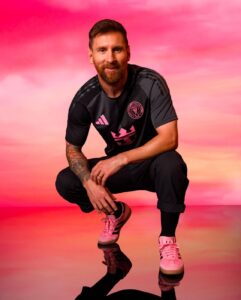 Man in black athletic outfit crouching on a pink gradient backdrop, facing the camera with a slight smile