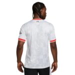 Back view of a white sports jersey with red and yellow striped sleeve cuffs and a small logo near the neckline, worn by a man with braided hair.