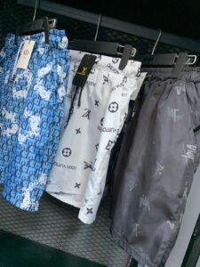 Row of Louis Vuitton branded rain pants on hangers in a store, featuring blue patterned pair, white logo print pair, and dark gray pair with tags visible in front.