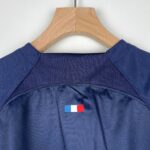 Navy blue shirt on a wooden hanger with a small French flag patch visible at the bottom center of the garment.