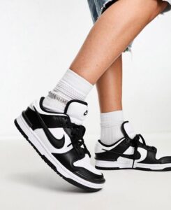 Close-up of feet in white crew socks wearing black-and-white Nike sneakers on a light floor; mid-step pose.