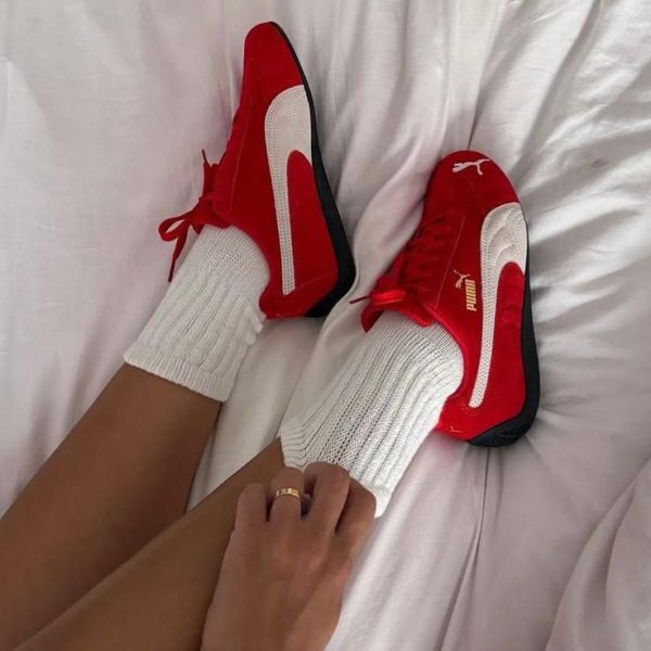 Red Puma sneakers with white stripes worn with thick white socks, resting on a white bedspread.