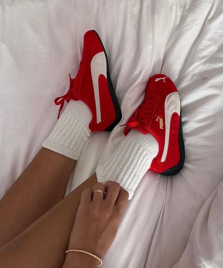 8b2daa6a-460a-443f-932b-f5933a45b321 | UAE SPORT STORE Red Puma sneakers with white stripes worn with thick white socks, resting on a white bedspread.