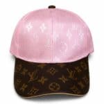 Pink baseball cap featuring a white Louis Vuitton monogram pattern on the crown and a brown LV-patterned brim.