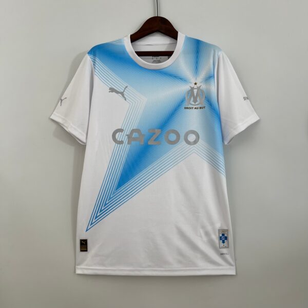 White and blue soccer jersey hanging on a wooden hanger, with OM crest, Puma logo, and sponsor text visible across the chest.