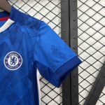 Close-up of a blue Chelsea FC jersey sleeve with crest visible, against a metal fence background.