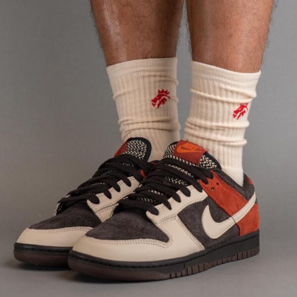 Pair of cream, black, and red sneakers with white Nike swooshes on a model wearing cream socks with red branding.