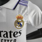 Close-up of a white sports jersey featuring the Real Madrid crest on the chest and purple trim at the collar.