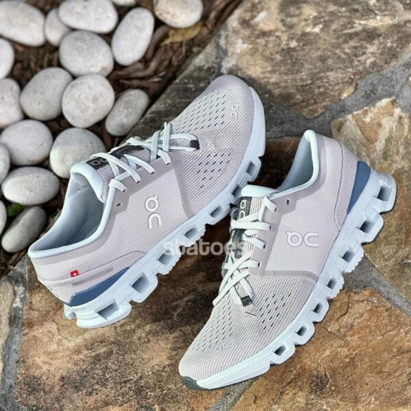 Pair of light gray On running shoes with perforated uppers and cloud-like midsole on a stone surface.