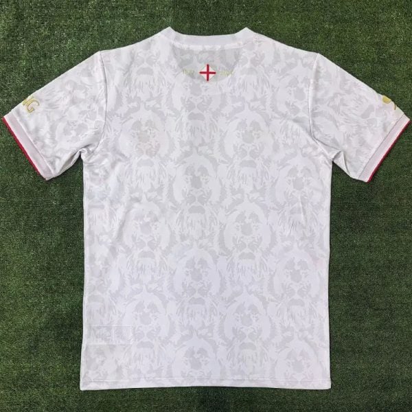 White patterned T-shirt laid flat on grass, back side up, with a small cross crest near the neckline.]','White back-view of a white short-sleeve shirt with a subtle damask pattern on green turf.
