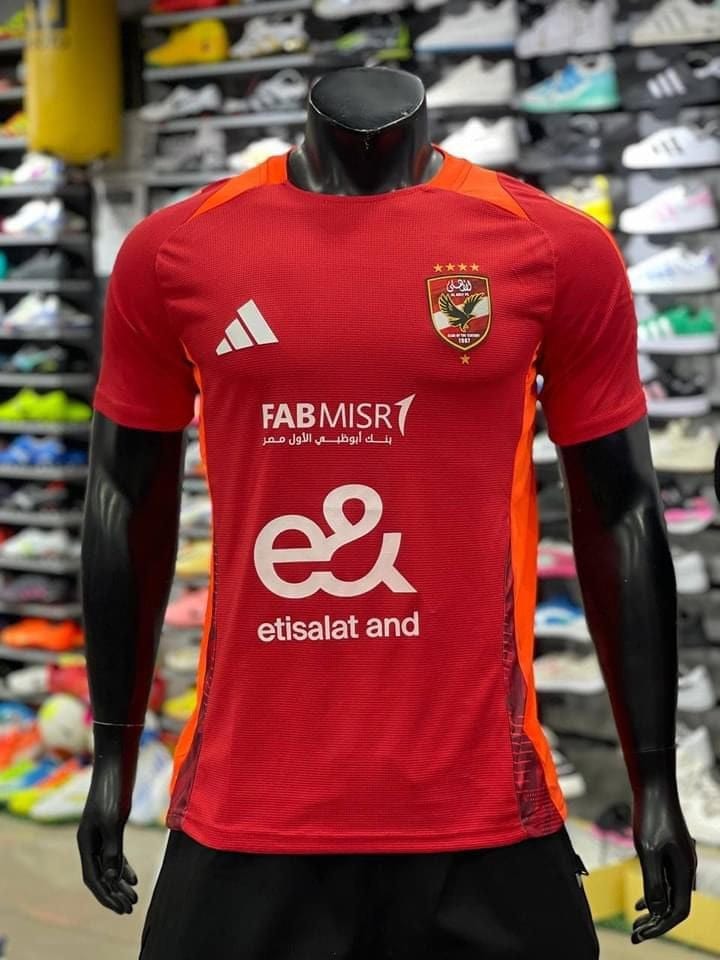 8d373fb4-0ed5-4e71-a17f-bcd229edfcba | UAE SPORT STORE Red football jersey on a black mannequin with team crest and sponsor logos, displayed in a shoe store