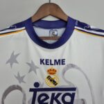 8dccd430_d05cbb00-5b9d-41da-b6b8-2412caccd5d6 | UAE SPORT STORE White Real Madrid football jersey on a wooden hanger, featuring purple trim and the club crest with a Kelme label visible in the collar area.