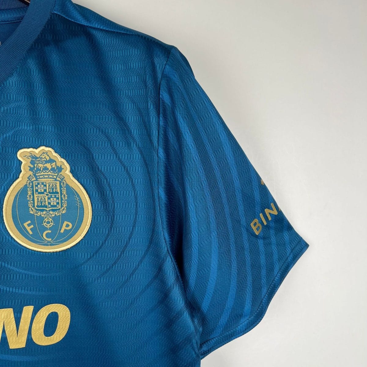 Close-up of a blue police uniform shirt showing a gold-bordered badge patch on the chest and partial gold lettering nearby.