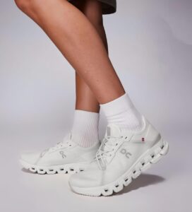 Side view of a person wearing white athletic sneakers and white crew socks, with one foot slightly ahead.