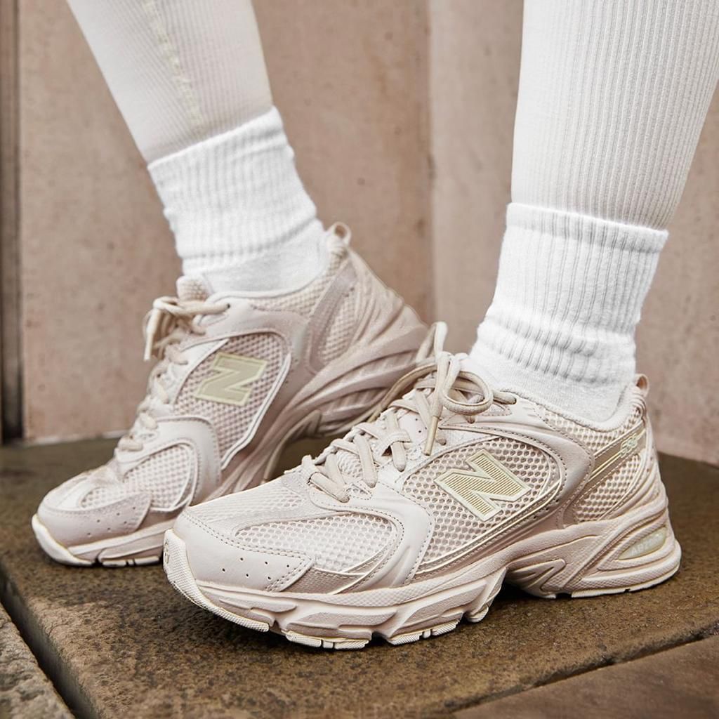 8e642d63-4327-4819-a68a-ebb7c8216d9b | UAE SPORT STORE Beige New Balance sneakers with a chunky sole, worn with white crew socks, standing on a stone step.