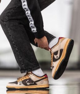 Person tying tan and black sneakers while wearing white socks and a black tracksuit with a white stripe on the leg