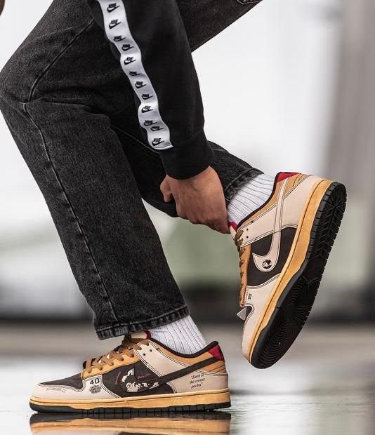 Person tying tan and black sneakers while wearing white socks and a black tracksuit with a white stripe on the leg