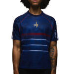 Person wearing a dark blue athletic jersey with a gold emblem on the chest and red trim details on the shoulders and sleeves.