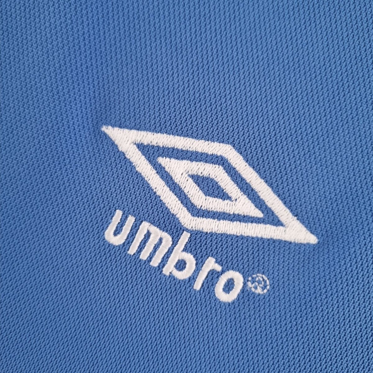 Close-up of blue denim fabric featuring white stitched logo element curved across the material