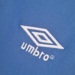 8ebc3e65_7804fdf0-da54-417f-992f-bf20a89014e5 | UAE SPORT STORE Close-up of blue denim fabric featuring white stitched logo element curved across the material