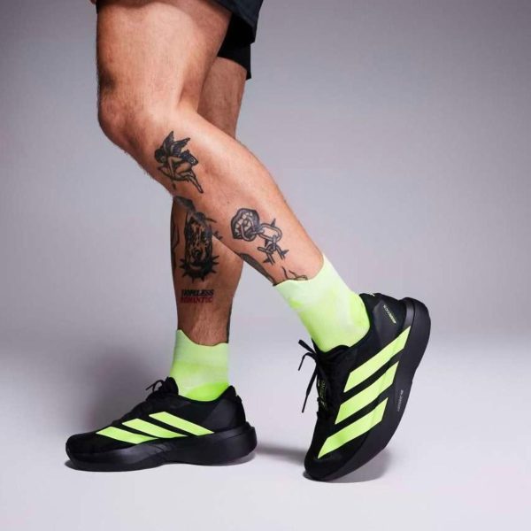 Legs wearing neon yellow socks and black sneakers with lime-green stripes, tattoos visible on the lower legs.